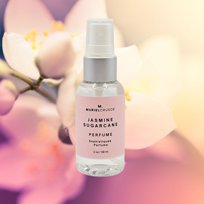 A spray bottle of JASMINE SUGARCANE PERFUME MIST with a pink label, placed against a blurred floral background.