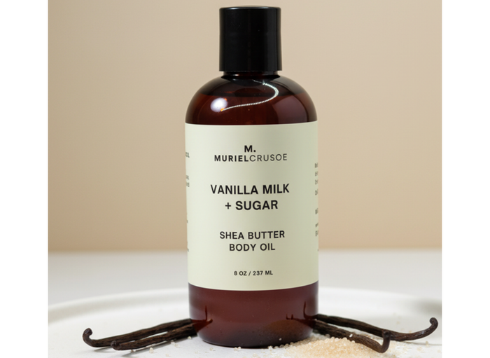 Shea butter body oil bottle labeled 'Vanilla Milk + Sugar' by M. Muriel Crusoe on a beige background.